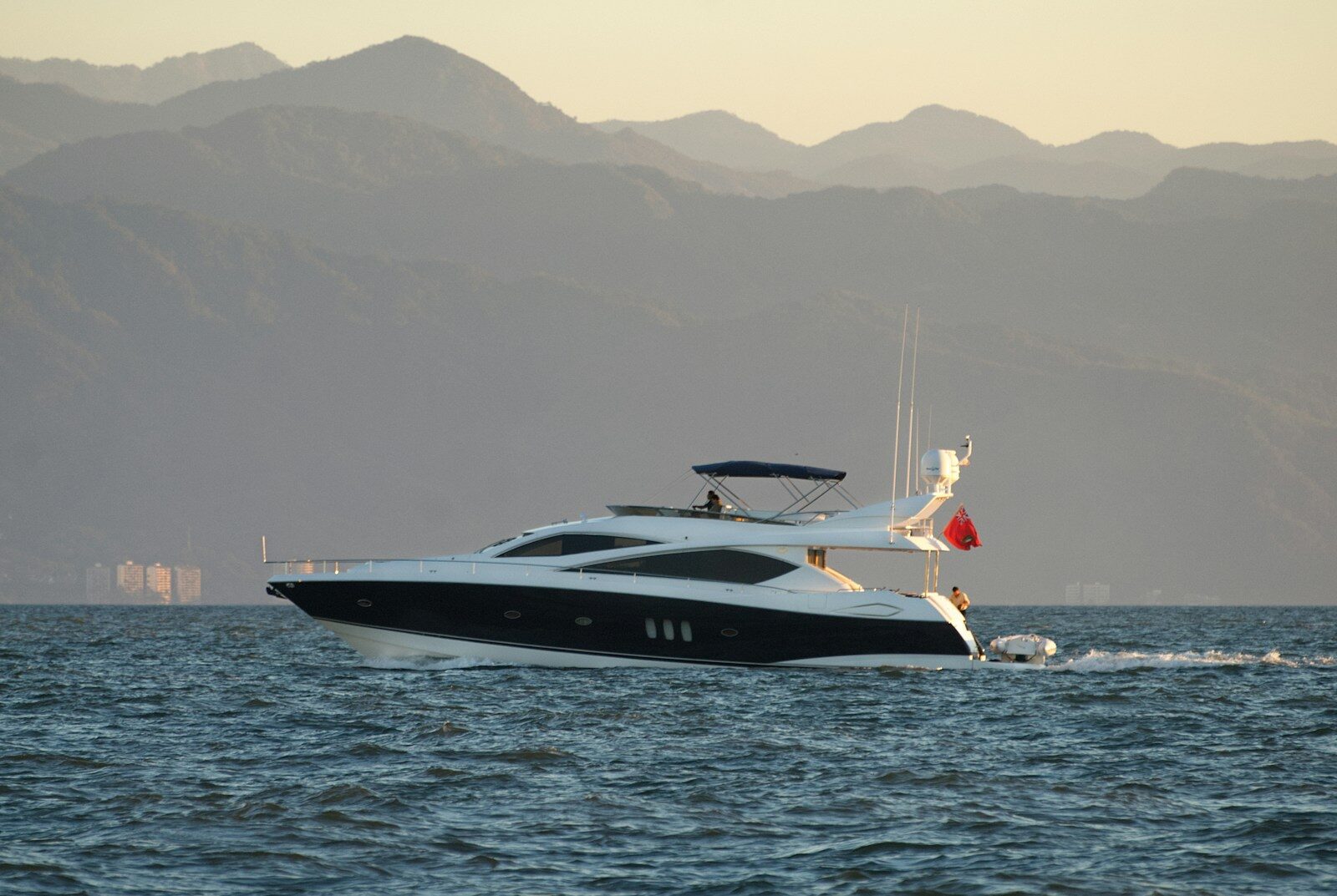 A sleek yacht sails on the ocean with mountains behind